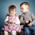 This is a post about social media engagement. The featured image is a photo of two toddlers, a boy and a girl. They're sitting together on a bench. Both have cell phones. She is looking intensely at the screen of her phone while he looks worriedly over her shoulder, trying to peek