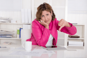 Photo shows an woman in a bright pink blazer, sitting at her desk. She is frowning and giving the thumbs down with her left hand. This is the featured image for a post titled "Nonprofit Branding: No One Cares About Your Logo"